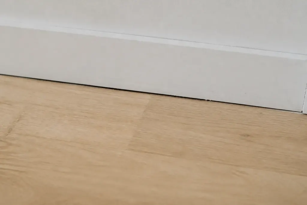 Fente visible entre parquet clair et plinthe blanche