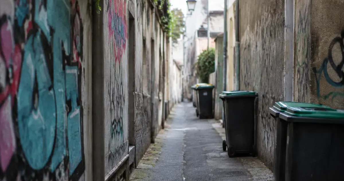 Rue étroite bordée de murs tagués et de poubelles
