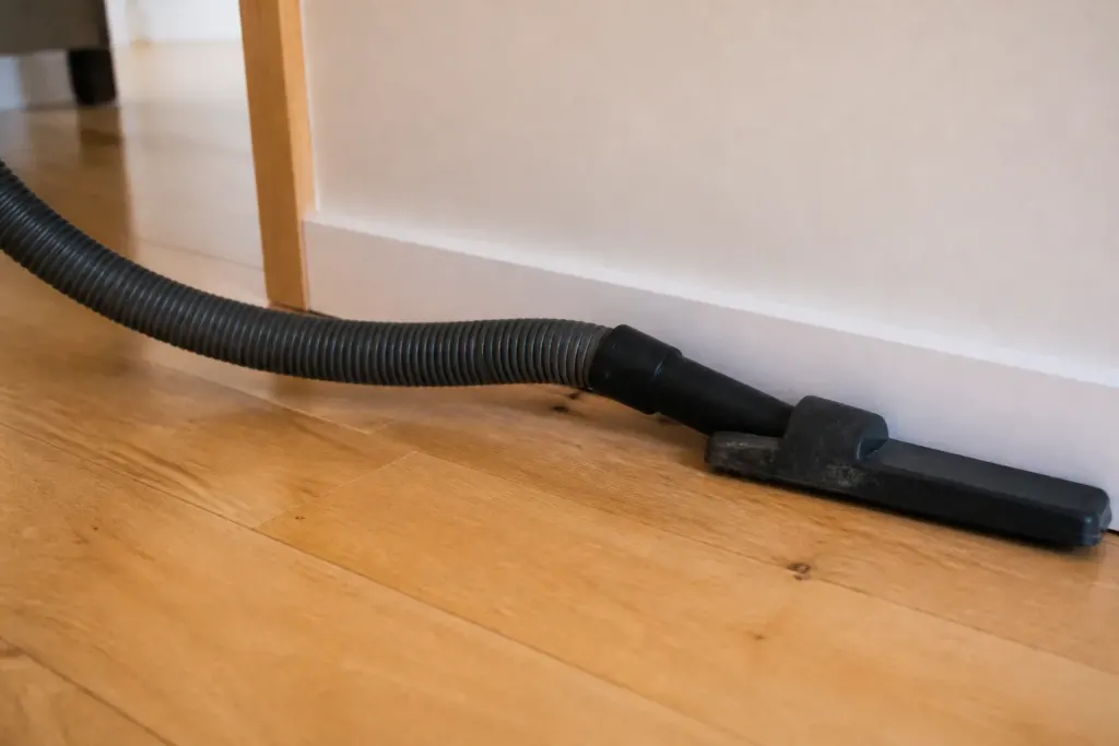 Tuyau aspirateur glissant sur parquet clair contre plinthe blanche